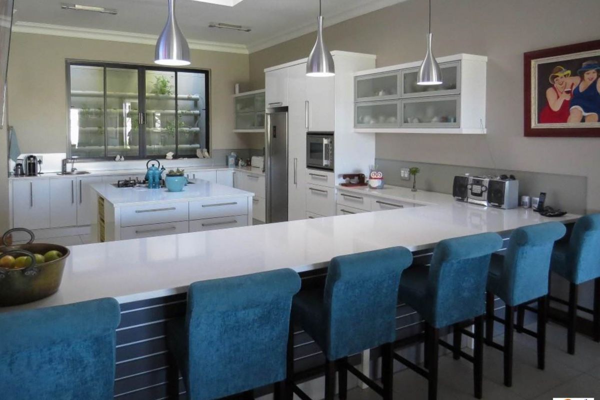 Modern kitchen featuring white cabinetry, stone countertops, a central island with a built-in hob, and a breakfast bar with pendant lighting.