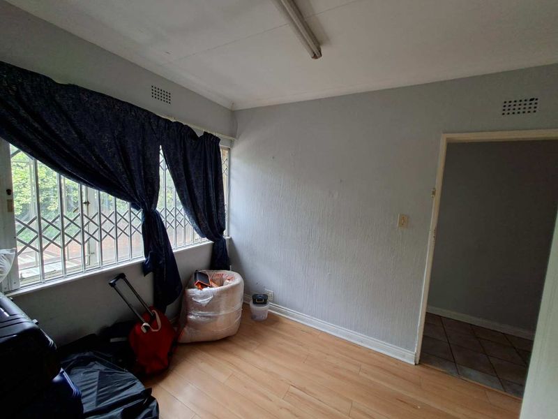 A vacant bedroom featuring laminate flooring, a security gate on the window, and neutral wall finishes, ready for a fresh update.