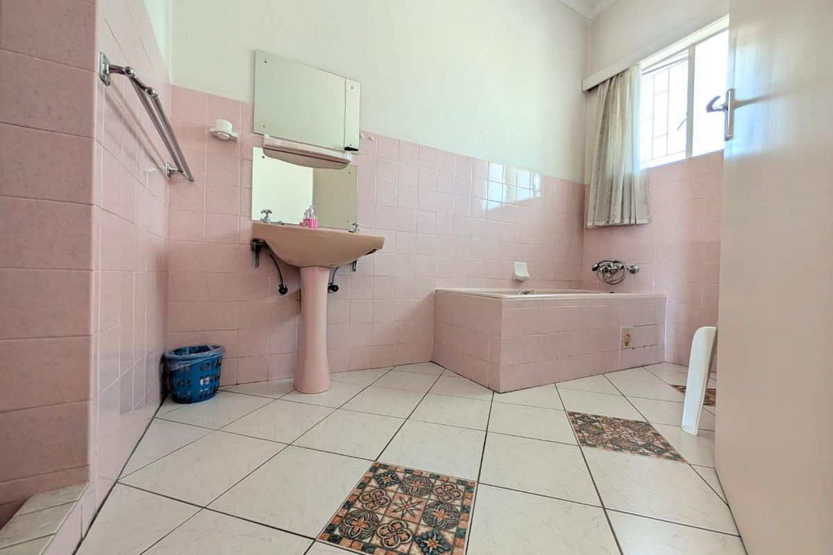A dated bathroom featuring original pink wall tiles, a matching pink pedestal basin, and a built-in tiled bathtub with decorative floor tile accents.