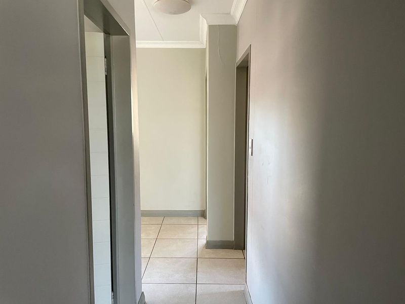 A neutral-toned hallway featuring tiled flooring, ceiling cornice, and access to multiple rooms, presenting a clean and functional transition space.