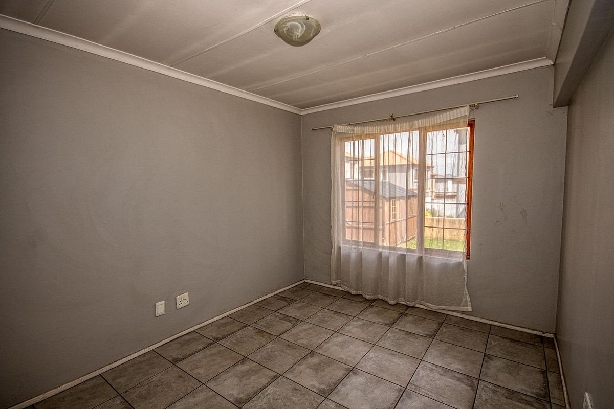 A vacant bedroom featuring neutral grey walls, tiled flooring, and a large window providing natural light.