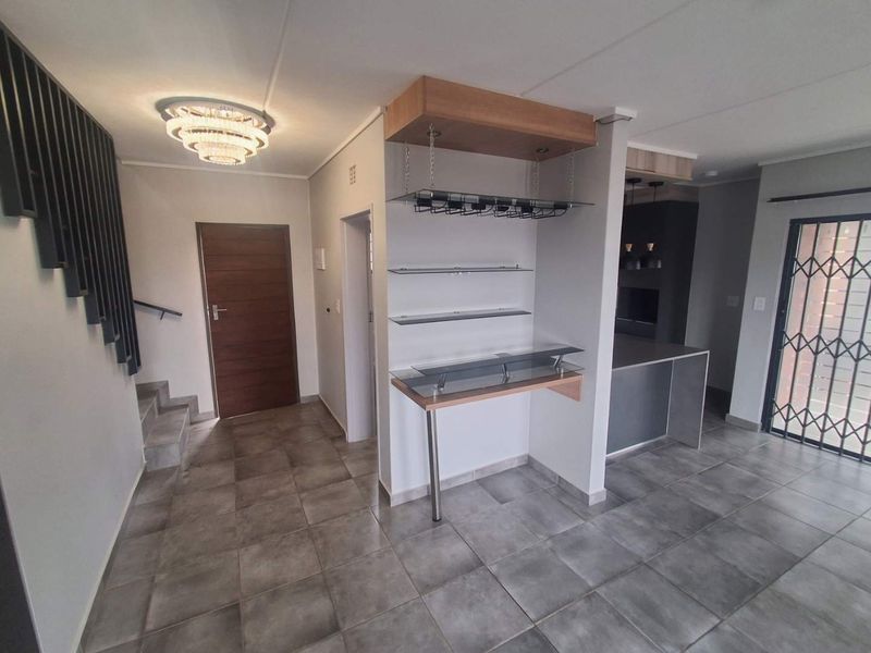 Open plan living area featuring a built-in bar with glass shelving, tiled flooring, and a staircase leading to the upper level.