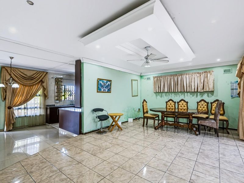 Spacious open-plan living and dining area featuring tiled flooring, a decorative recessed ceiling with a fan, and an adjoining kitchen space.
