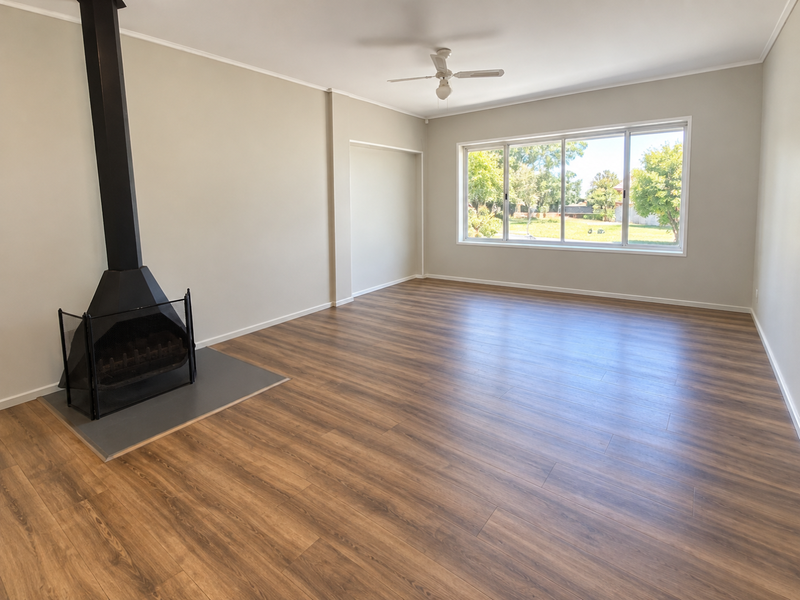 Spacious, light-filled living room featuring modern laminate flooring, a freestanding fireplace, and a ceiling fan, offering a clean and neutral canvas.
