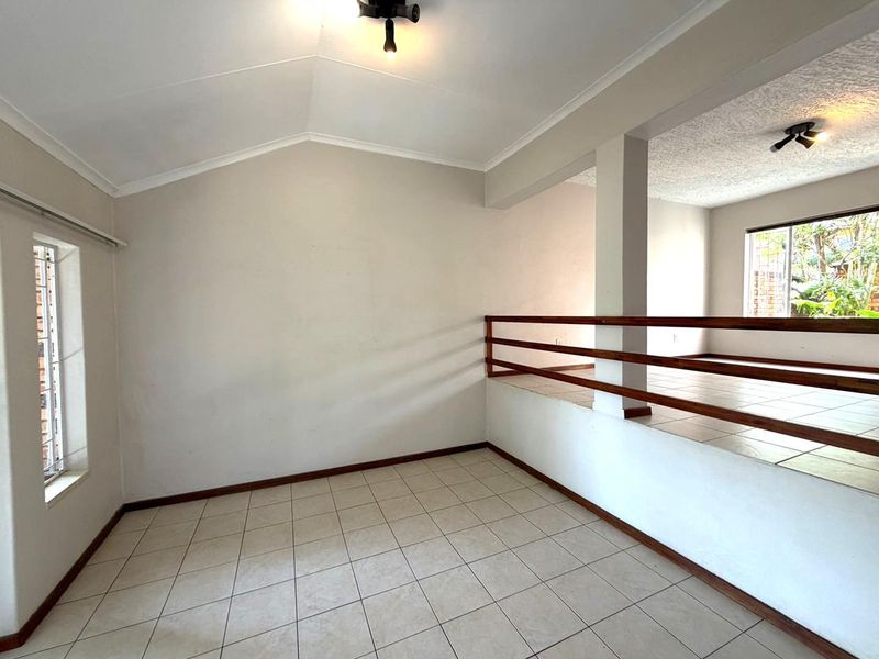 An empty, split-level living area featuring tiled flooring, a vaulted ceiling, and a timber balustrade, offering a versatile open-plan layout.