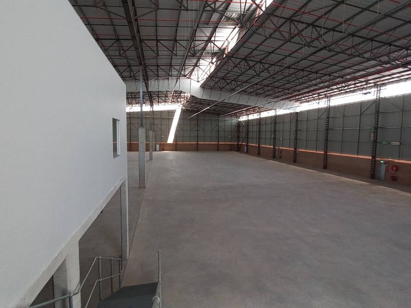 Spacious industrial warehouse featuring high ceilings with exposed steel trusses, concrete flooring, and a mezzanine level, suitable for various commercial or storage operations.