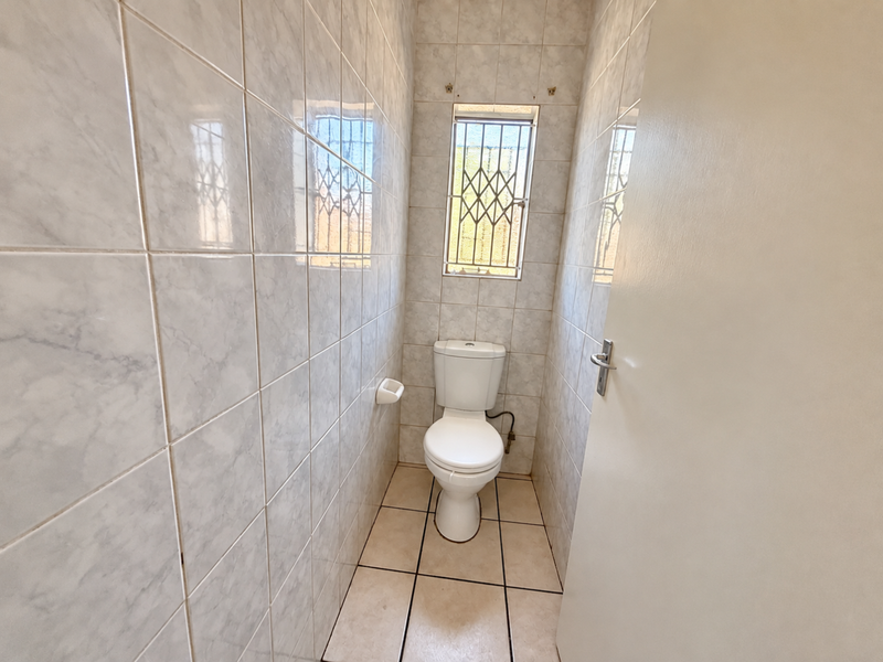 A compact, tiled guest toilet featuring a standard white toilet suite and a window with security bars.