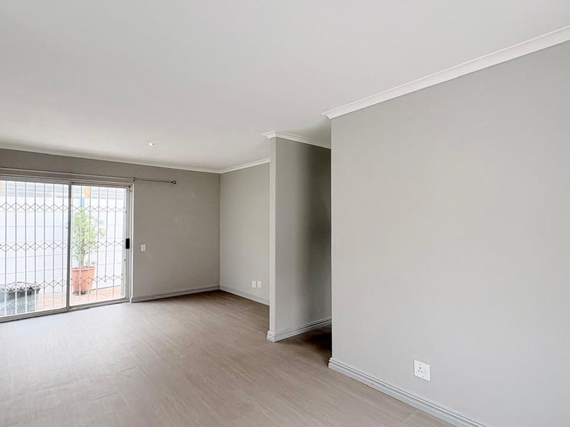 A bright, empty living room featuring neutral grey walls, laminate flooring, and a sliding glass door with a security gate leading to the exterior.