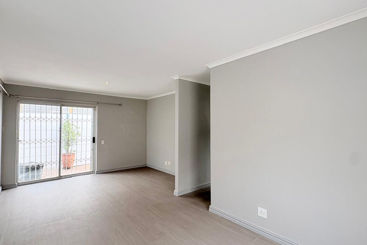 A bright, empty living room featuring neutral grey walls, laminate flooring, and a sliding glass door with a security gate leading to the exterior.