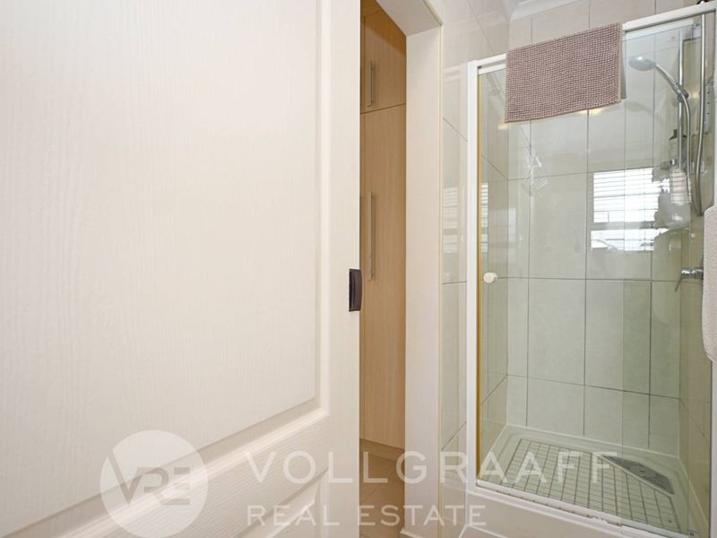 A functional bathroom featuring a glass-enclosed shower with tiled walls and adjacent built-in cabinetry for storage.