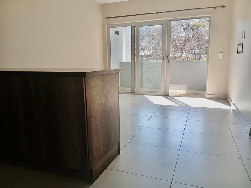 An empty open-plan living area featuring tiled flooring, a kitchen island, and sliding glass doors leading to a balcony.