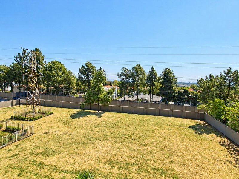An elevated view overlooking a large open grass area enclosed by a perimeter wall, featuring a prominent electrical pylon and surrounding trees.