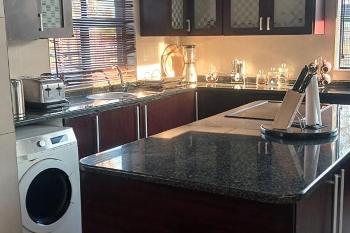 Modern kitchen featuring dark wood cabinetry, granite countertops, a central island, and integrated laundry appliance space.