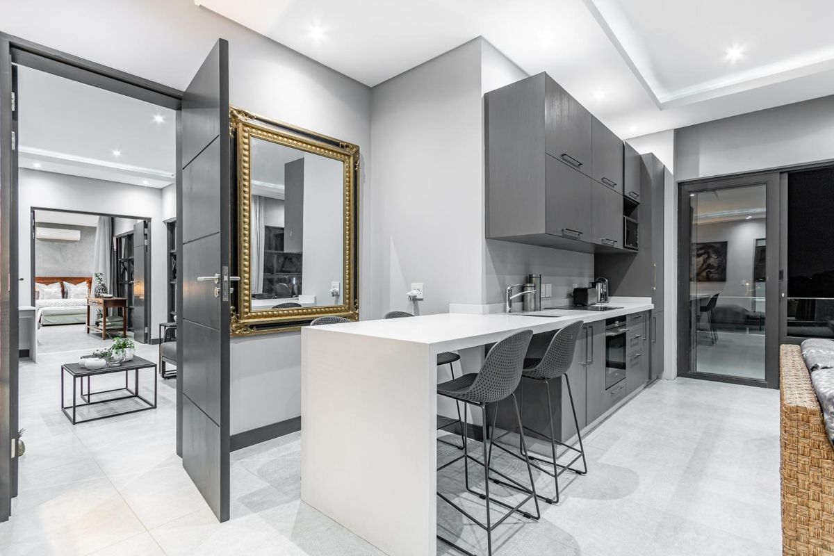 Modern kitchen featuring sleek grey cabinetry, integrated appliances, and a breakfast bar, seamlessly flowing into the adjacent living area.