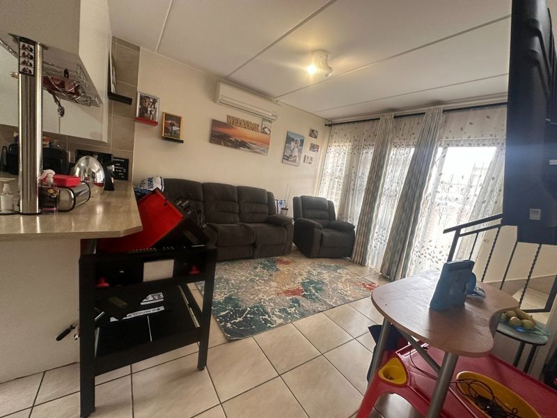 Open-plan living area featuring tiled flooring, a split-system air conditioner, and an integrated kitchen space with direct access to the staircase.