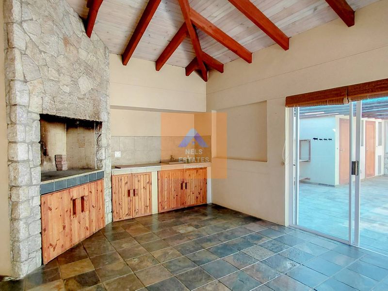 Covered patio area featuring a built-in stone braai, exposed timber rafters, and tiled flooring, with sliding glass doors leading to an outdoor space.