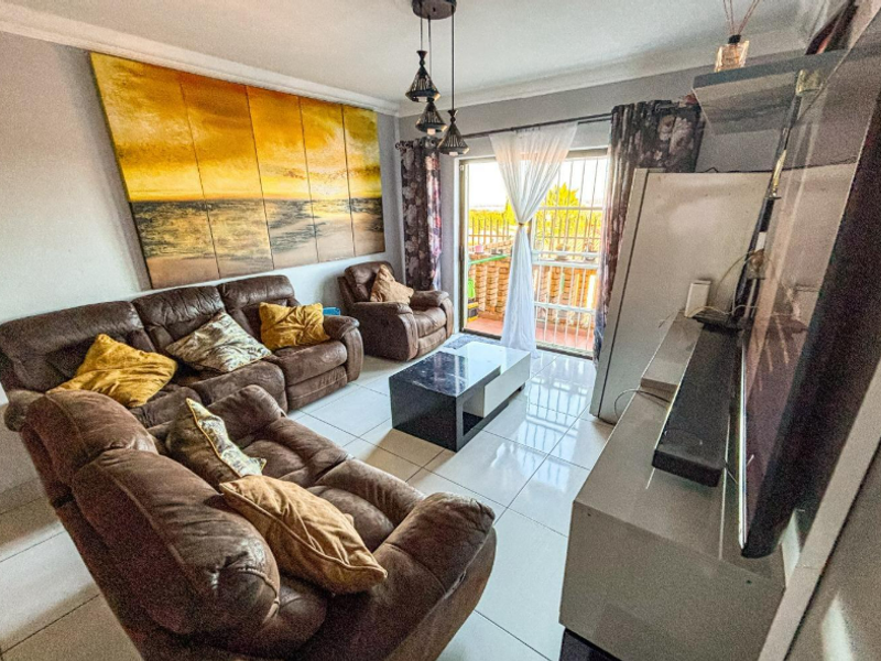 A comfortable living room featuring tiled flooring, cove cornicing, and a sliding glass door providing access to an outdoor balcony area.