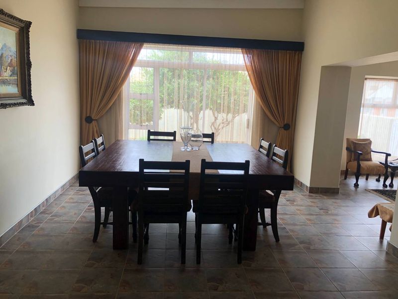 A spacious dining room featuring large windows with curtains, tiled flooring, and high ceilings, providing a bright and functional space for family meals.