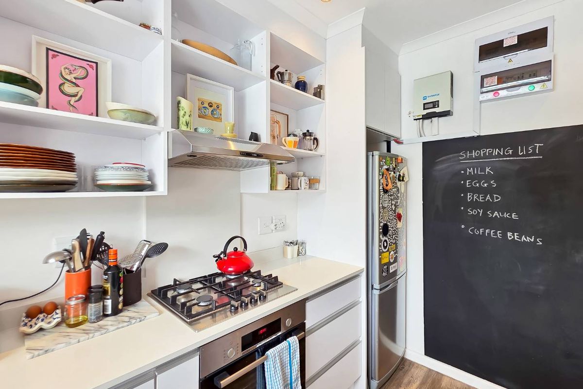 Modern kitchen featuring white cabinetry, open shelving, gas hob, built-in oven, and a functional chalkboard wall for daily organization.