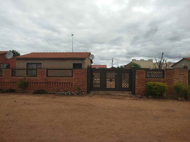 Front view of the property featuring a brick boundary wall, secure metal gate, and tiled roof structure.