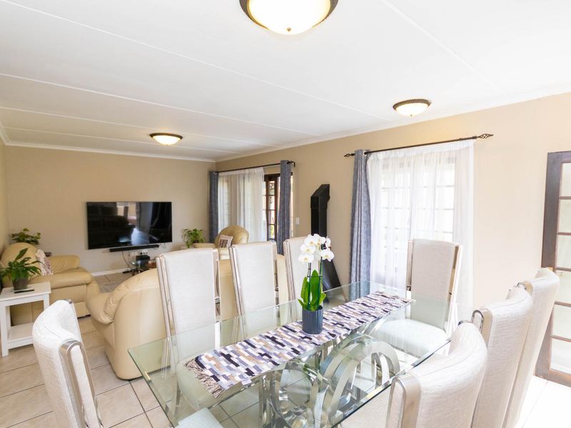 Spacious open-plan living and dining area featuring tiled flooring, a freestanding fireplace, and natural light through large windows and french doors.