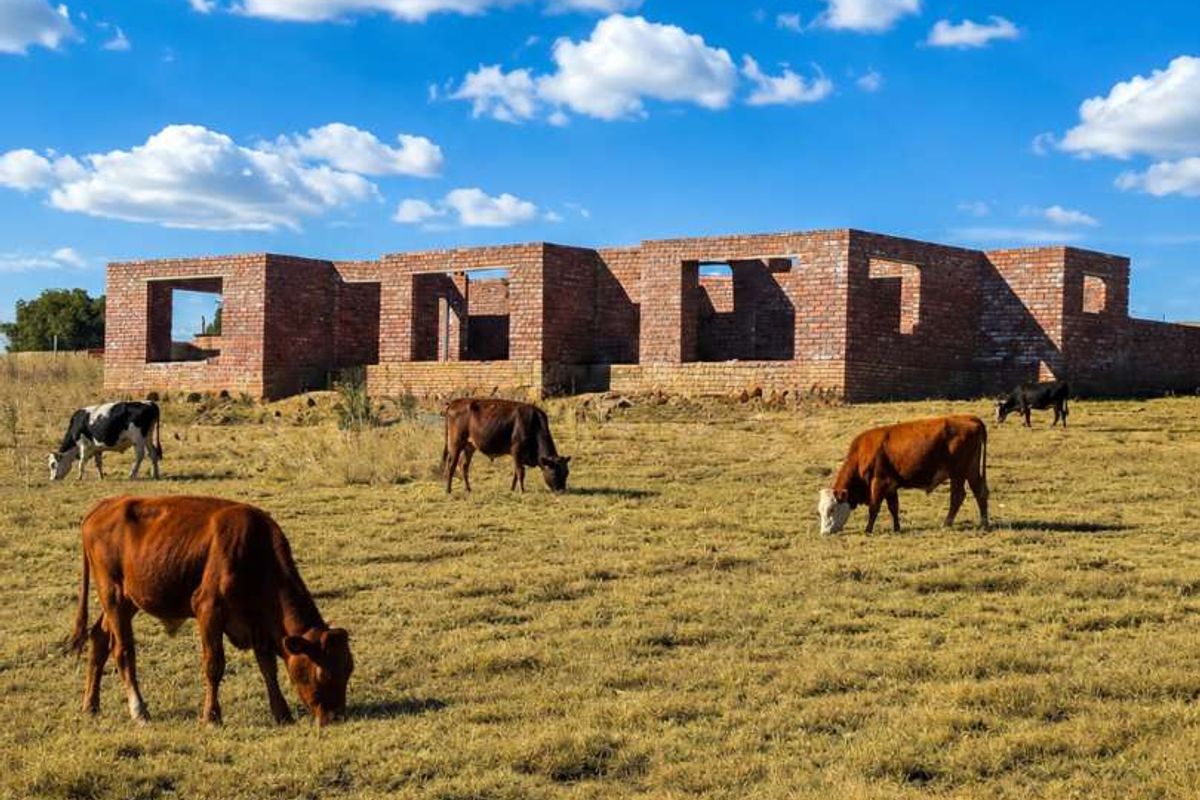 An unfinished brick structure set within a rural farm landscape, currently in the early stages of construction with open wall apertures.