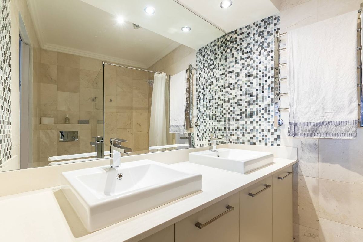 Modern bathroom featuring a double vanity with vessel sinks, mosaic tile backsplash, large wall-to-wall mirror, and a glass-enclosed shower area.