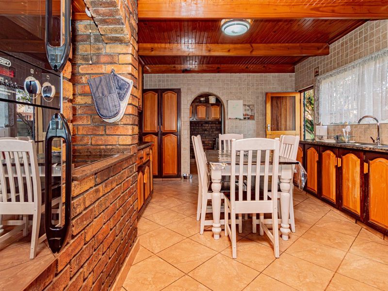 A rustic kitchen featuring exposed brick walls, timber ceiling beams, granite countertops, and wooden cabinetry with a dedicated dining area.