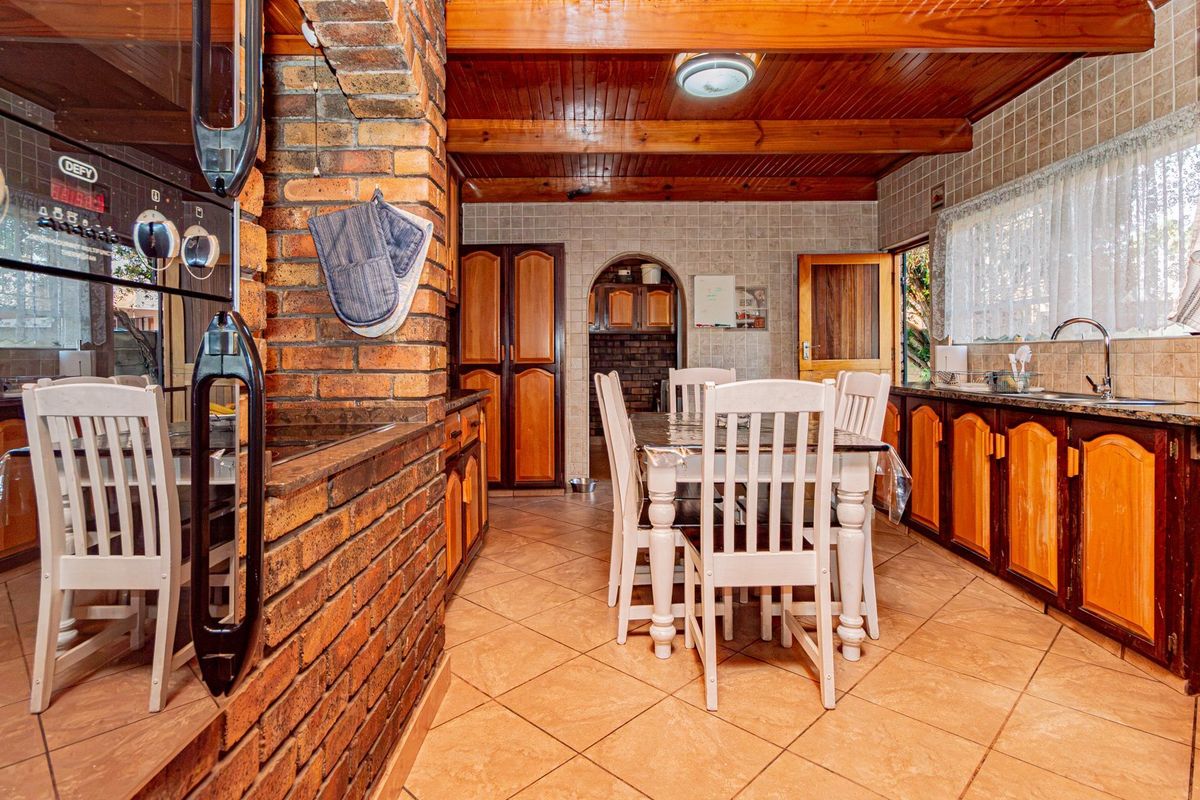 A rustic kitchen featuring exposed brick walls, timber ceiling beams, granite countertops, and wooden cabinetry with a dedicated dining area.