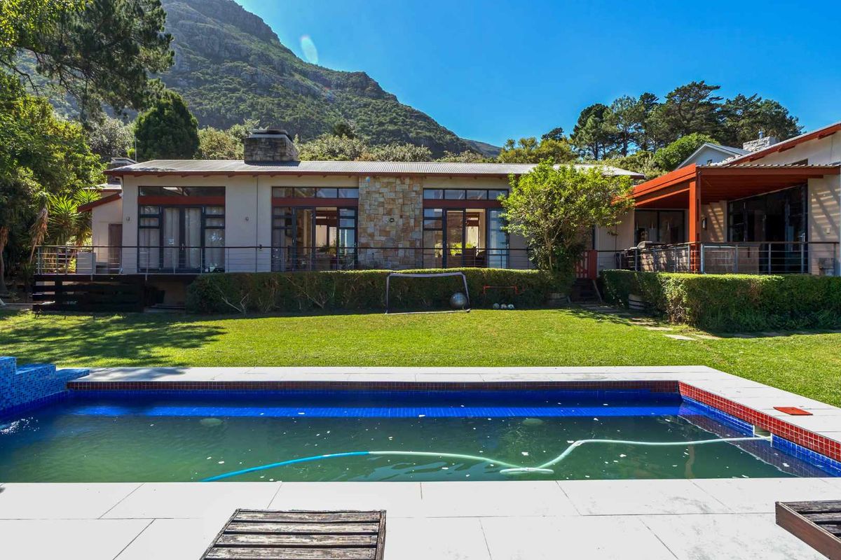 Rear view of the property featuring a swimming pool, landscaped garden, and a covered patio area set against a mountain backdrop.