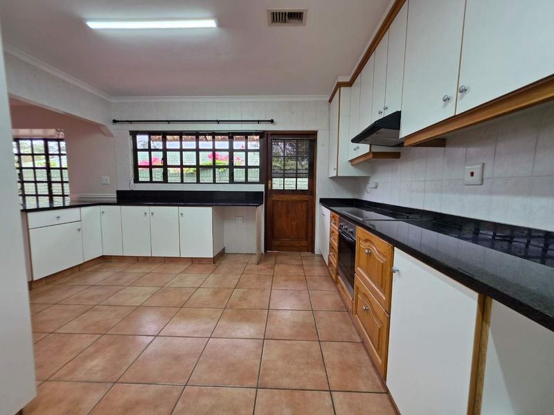 Spacious kitchen featuring built-in cabinetry, granite countertops, integrated oven and hob, and tiled flooring with direct access to the exterior.