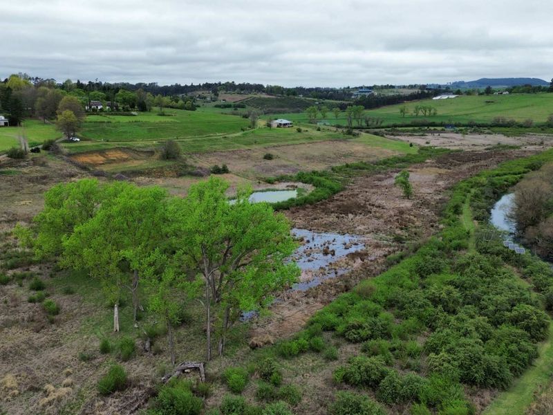 An aerial view of a large residential vacant land parcel featuring natural wetlands, a flowing watercourse, and established greenery in a rural setting.