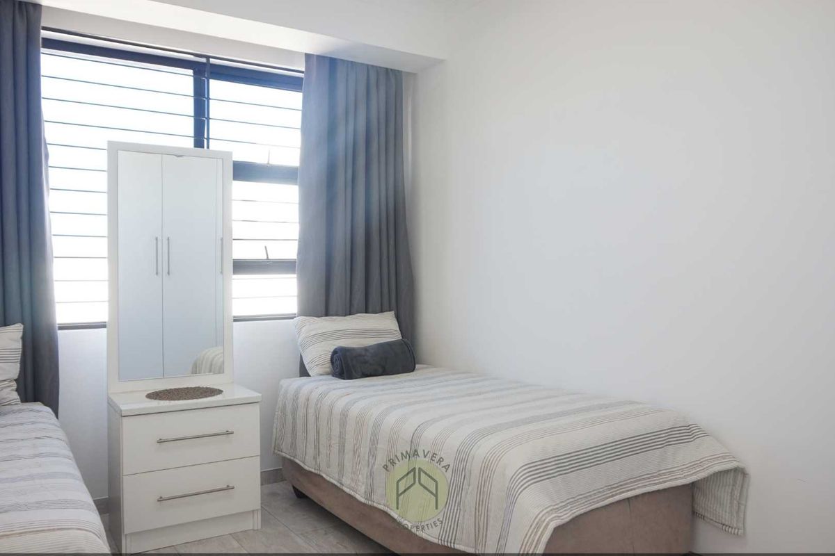 A bright bedroom featuring tiled flooring, large windows with fitted curtains, and neutral wall finishes.