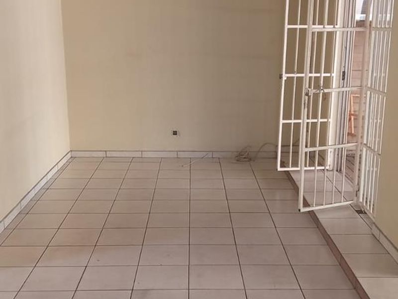 An empty living room featuring tiled flooring, a recessed ceiling, and a white security gate leading to an outdoor area.