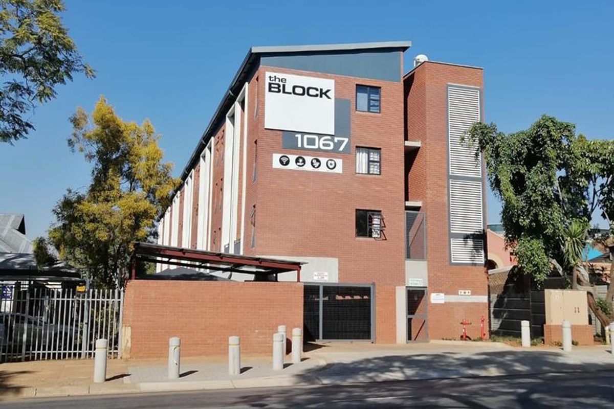 Street-facing view of The Block apartment complex, featuring a modern brick facade, secure gated entrance, and perimeter security fencing.