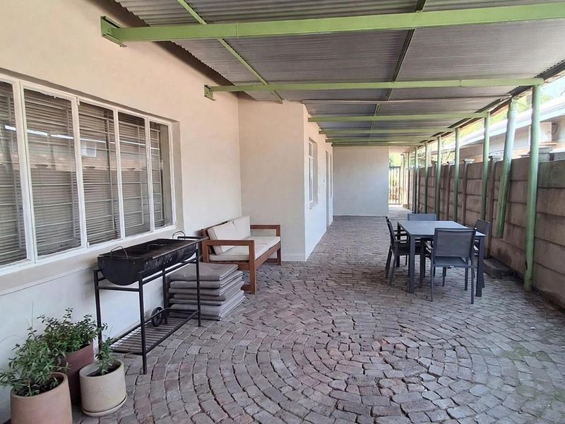 A covered outdoor patio area featuring paved flooring, a corrugated metal roof structure, and a precast concrete boundary wall.