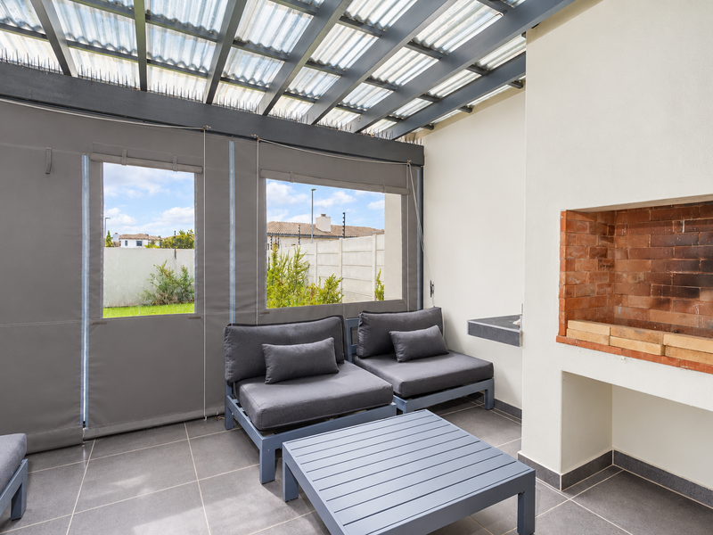 A covered patio featuring a built-in brick braai, tiled flooring, and retractable outdoor blinds, providing a functional space for outdoor entertaining.