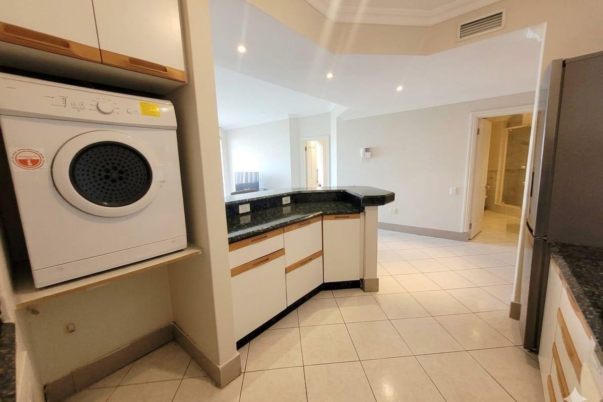 A functional kitchen featuring granite countertops, built-in cabinetry, and tiled flooring, with an open-plan layout leading to the living area and bathroom.