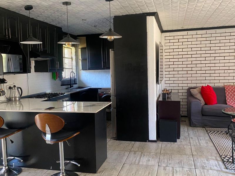 Open-plan kitchen and living area featuring modern black cabinetry, stone countertops, gas hob, and a distinctive white exposed brick feature wall.