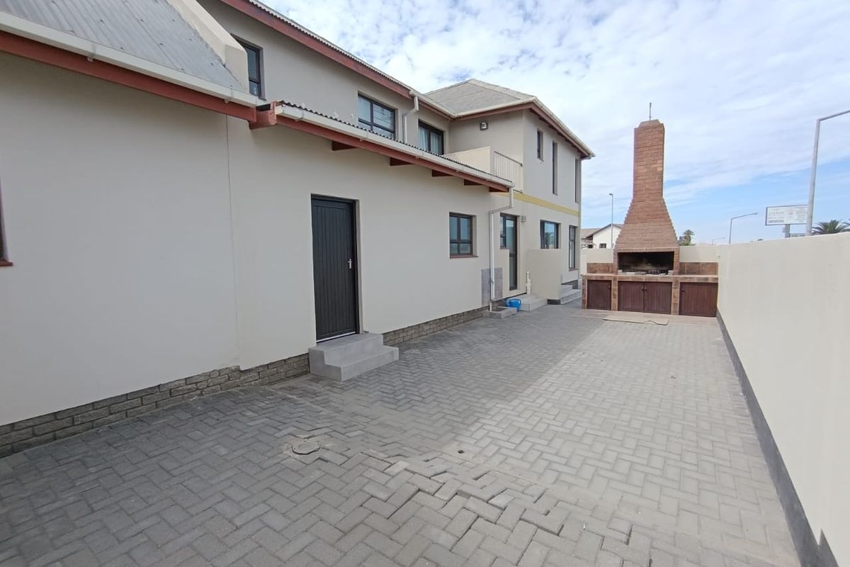 Rear exterior view of the townhouse featuring a paved courtyard, built-in brick braai area, and access to the main dwelling.