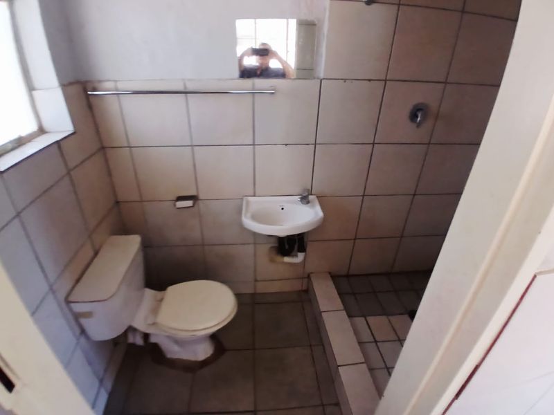 A compact bathroom featuring a toilet, wall-mounted basin, and a tiled shower area, requiring cosmetic updates to improve its overall condition and appeal.