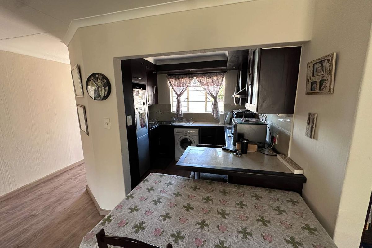 Compact kitchen featuring dark built-in cabinetry, laminate countertops, and integrated laundry plumbing, opening into a dining area with laminate flooring.