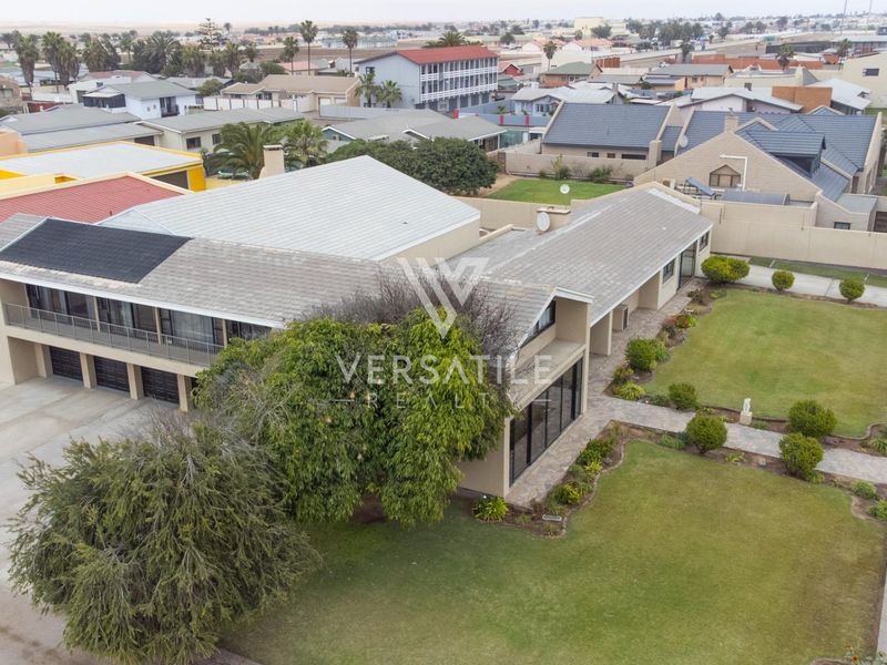 Aerial view of a residential property featuring a tiled roof with solar panels, a paved driveway, and a well-maintained garden.