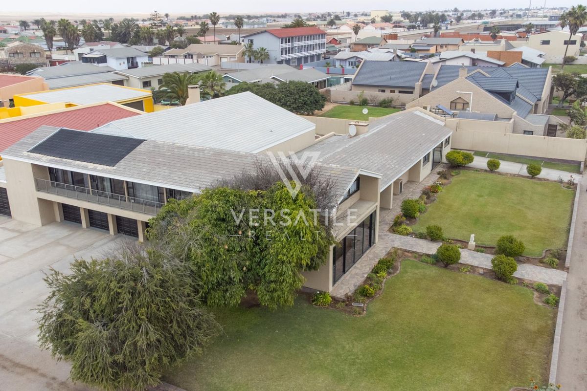Aerial view of a residential property featuring a tiled roof with solar panels, a paved driveway, and a well-maintained garden.