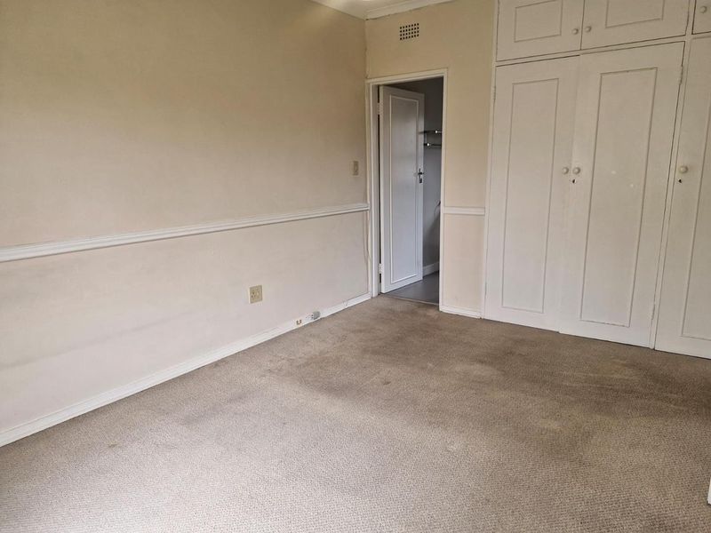 An empty bedroom featuring built-in cupboards, carpeted flooring, and classic chair rail molding, offering a blank canvas for renovation.