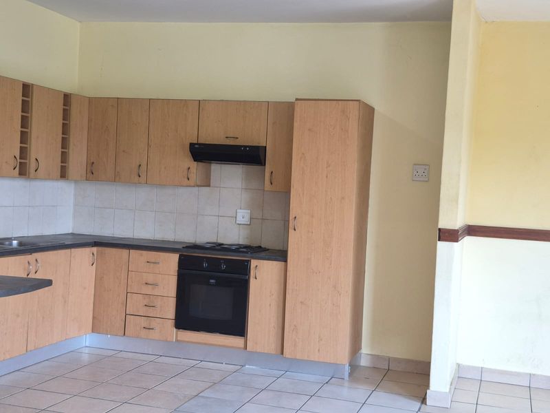 A functional kitchen featuring light wood-look laminate cabinetry, built-in oven, hob, extractor fan, and tiled flooring, offering a clean and practical layout.