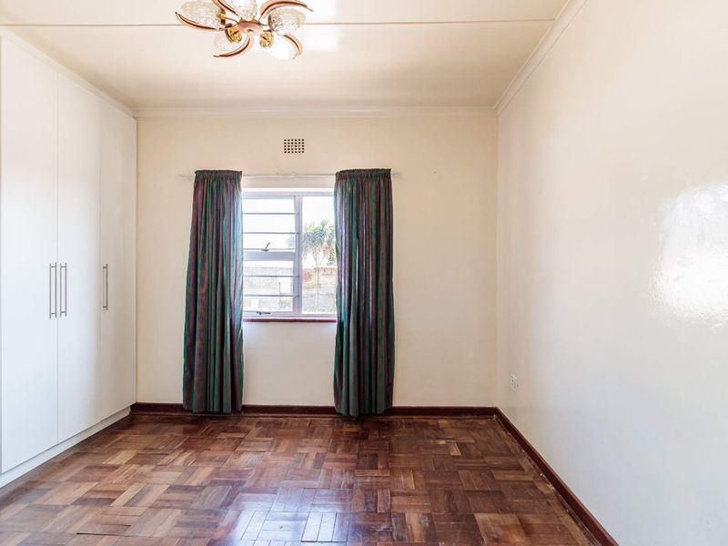 A bright, empty bedroom featuring classic parquet flooring, built-in cupboards, and a metal-framed window, offering a clean canvas for personalization.