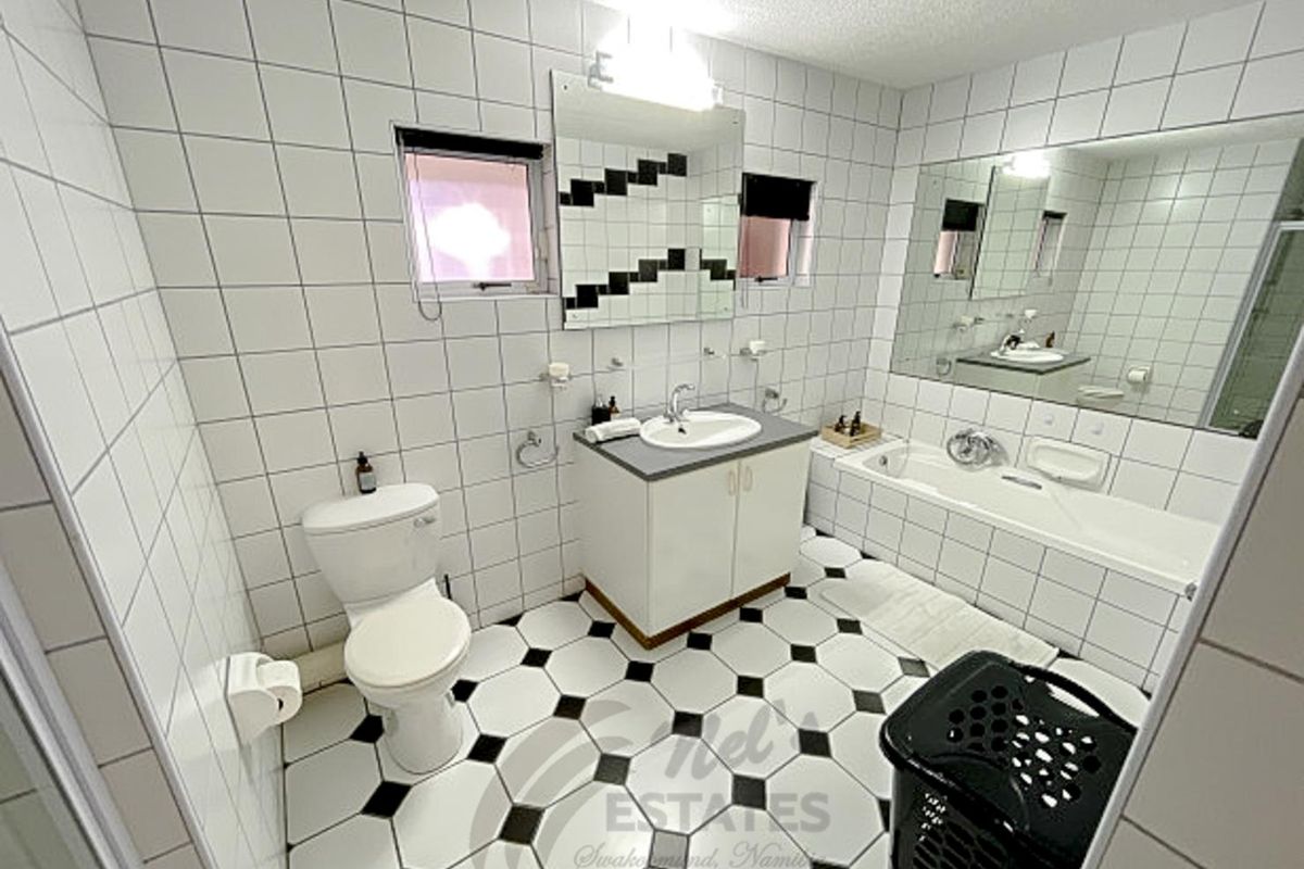 A functional bathroom featuring a vanity with basin, a bathtub, and a toilet, finished with classic black and white tiled flooring and wall accents.