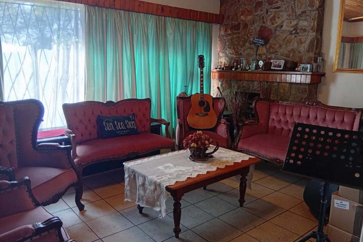 A living room featuring a prominent stone fireplace with a wooden mantelpiece and ceramic tiled flooring.