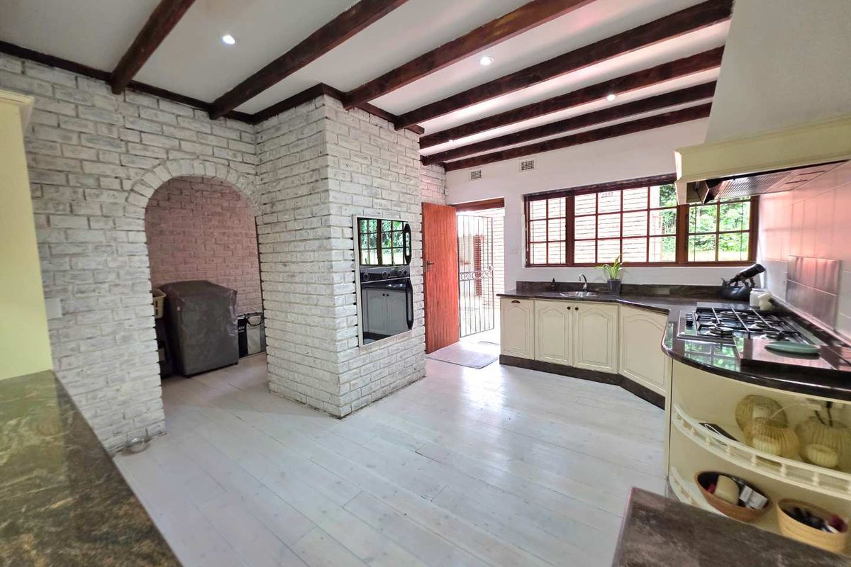 Spacious kitchen featuring exposed timber ceiling beams, white-painted brickwork, built-in oven, gas hob, and a separate scullery area with direct outdoor access.